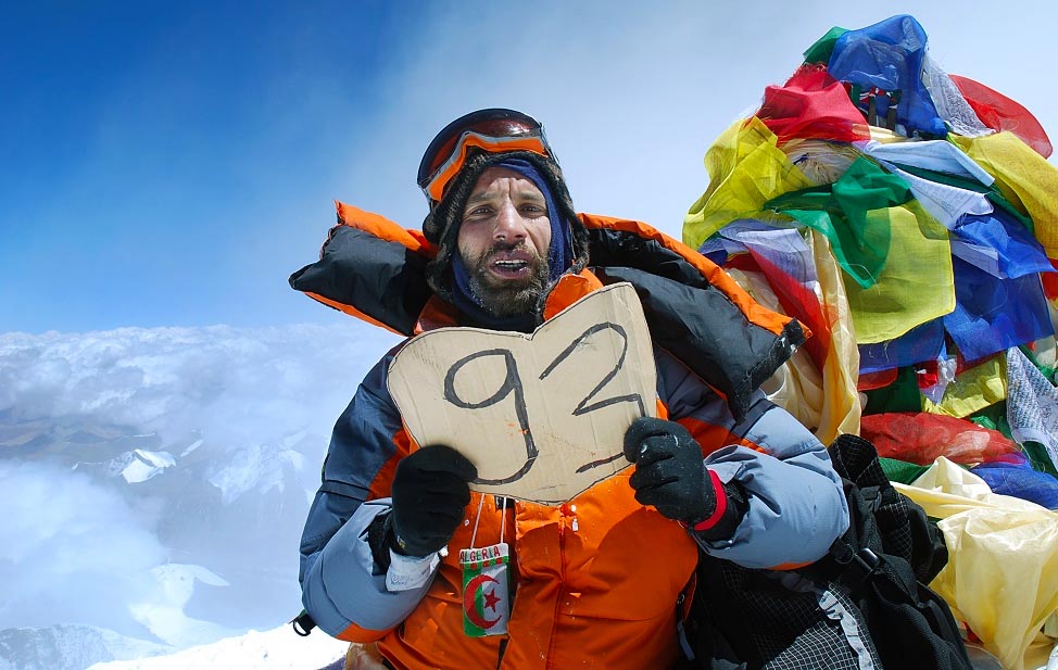 Nadir Dendoune holding up a cardboard sign with number 93 while atop Mt. Everest