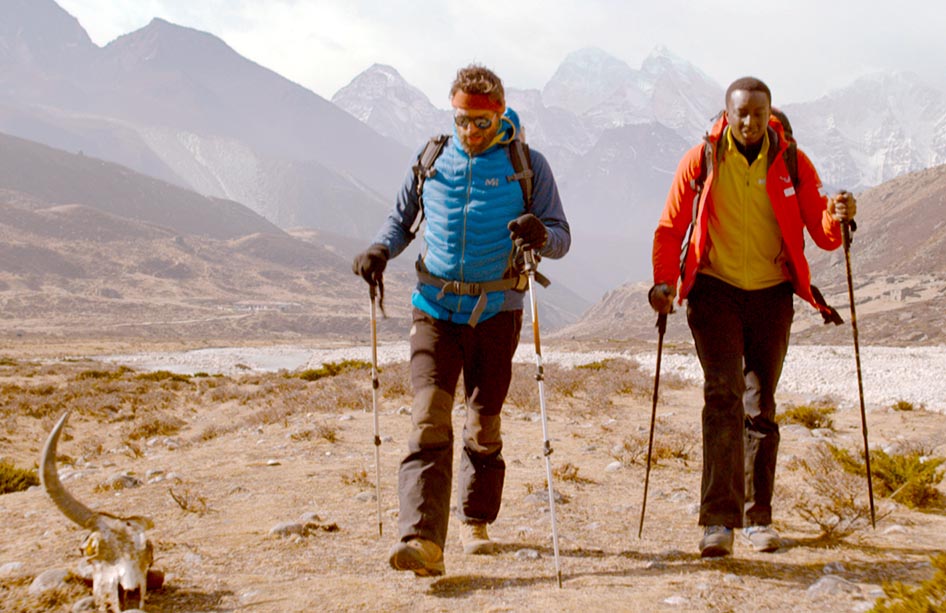 Samy and guide using walking poles as they walk towards Mt Everest in the film, The Climb